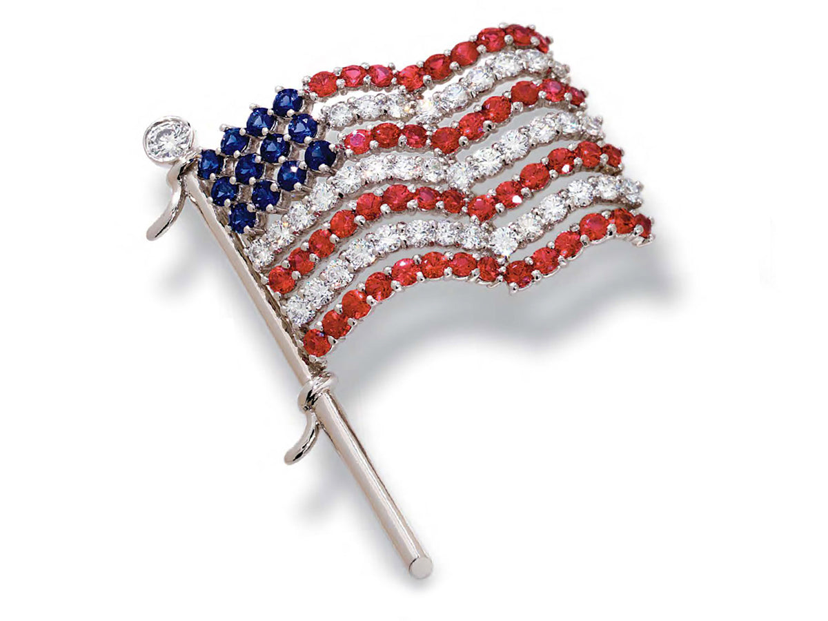 American flag brooch with red and blue gems and diamonds on white background.