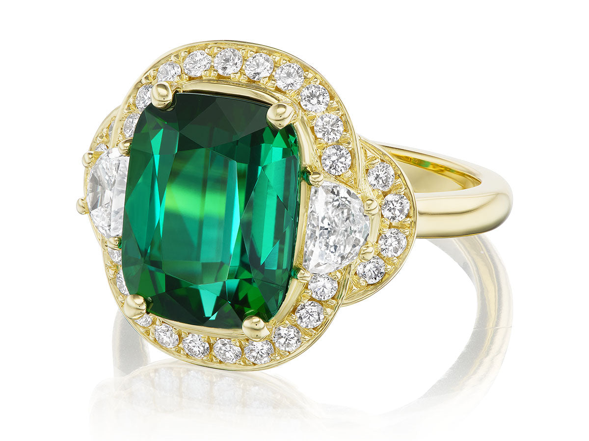 Gold ring with a green gemstone and diamonds on a white background