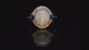 Video of rotating platinum ring with a star sapphire with two pear-shaped blue sapphires and diamonds on a black background.