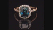 Video of rotating 20K pink gold ring with a cushion-cut teal sapphire and diamond halo on a black background.