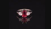 Video of rotating platinum ring with an emerald-cut ruby and two round diamonds on a black background.