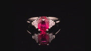 Video of rotating platinum ring with oval ruby and two half-moon diamonds on a black background