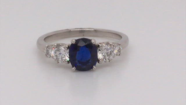 Video of rotating platinum ring with an oval sapphire with four diamonds on white background