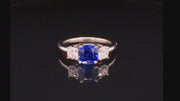 Video of rotating platinum ring with blue sapphire and round diamonds on black background.
