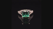 Video of rotating ring with green gemstone and diamonds on black background
