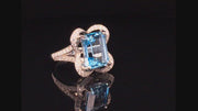 Video of rotating ring with blue gemstone and diamonds on black background