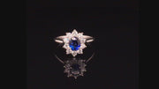 Video of rotating platinum ring with oval blue sapphire surrounded by brilliant diamonds on black background.