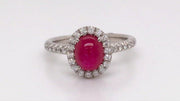 Video of rotating platinum ring with a ruby cabochon and diamond halo on a white background.