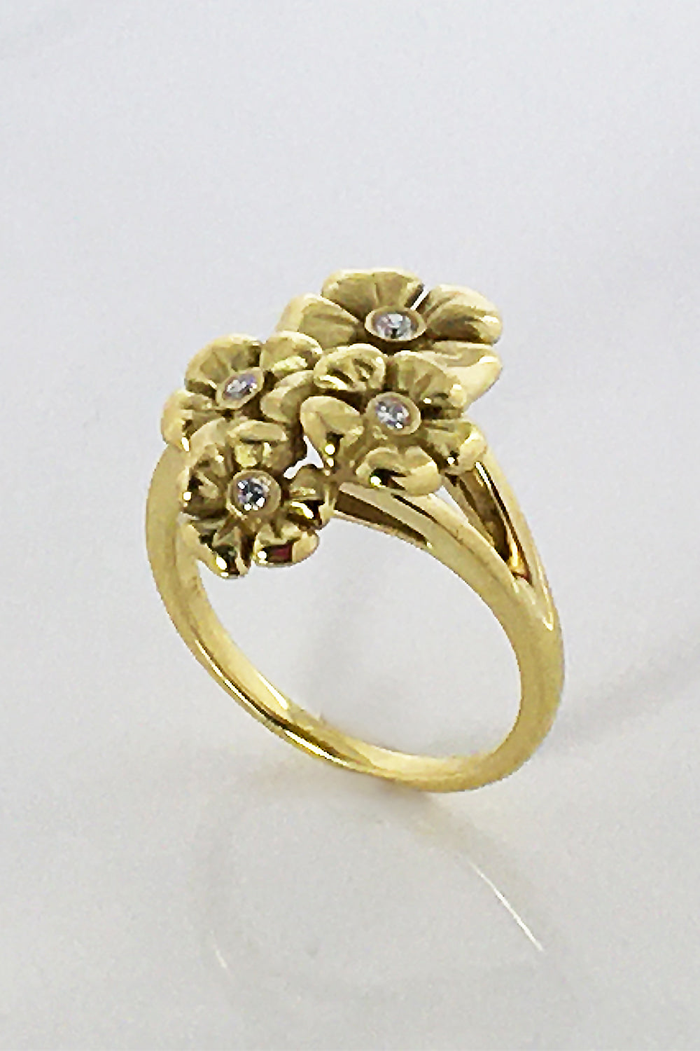 An 18KT yellow gold ring with a flower design and diamonds on white surface