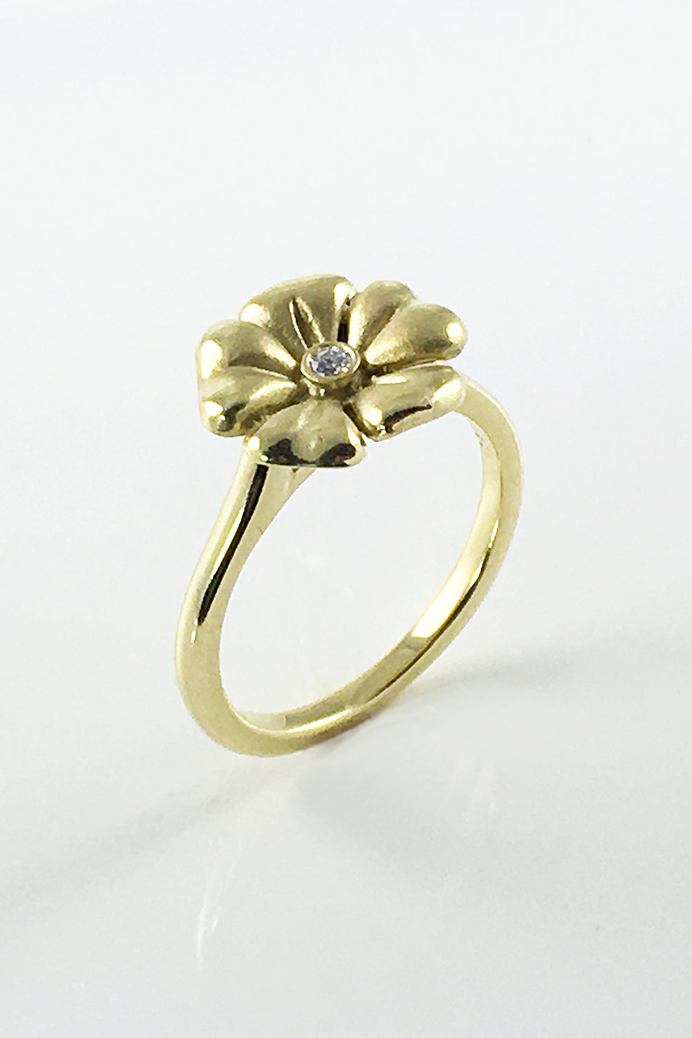 Angle view of an 18K yellow gold flower ring with a single diamond on a white surface
