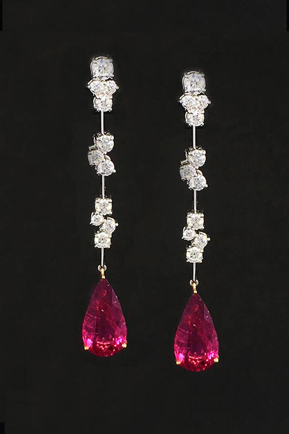 Drop earrings with diamond clusters on platinum wire and pear-shape rubellites on a black background