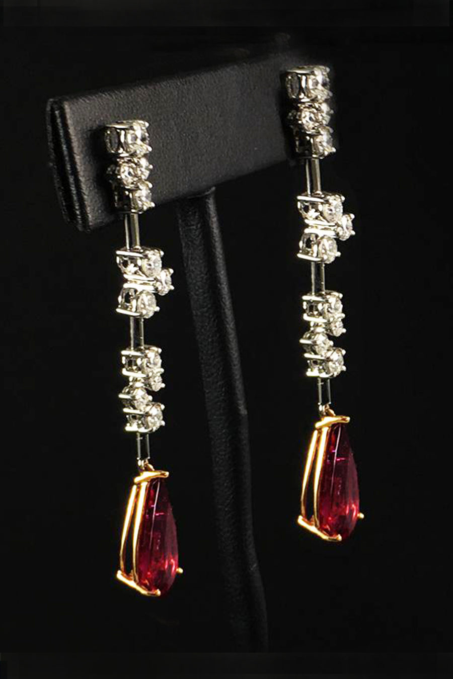 Side view of drop earrings with diamond clusters on platinum wire and pear-shape rubellites on a black background