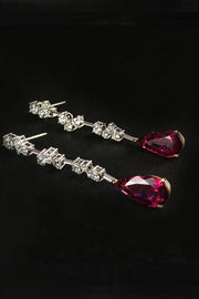 Drop earrings with diamond clusters on platinum wire and pear-shape rubellites laying down on a black background