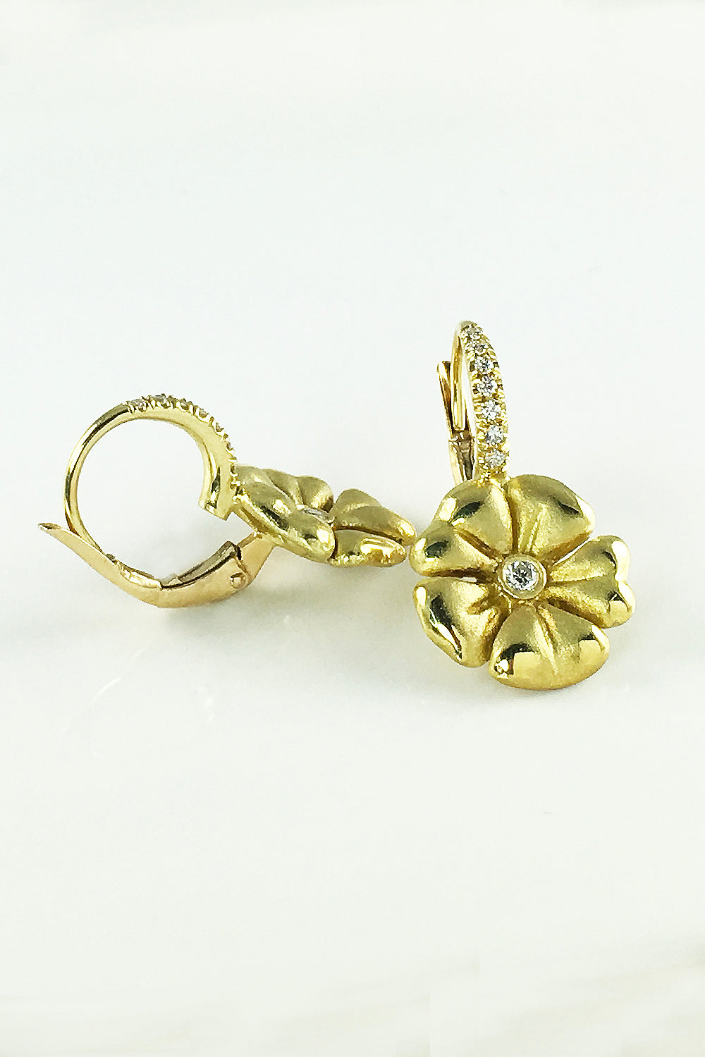 Side view of 18K yellow gold and diamond earrings featuring a flower motif and diamond lever backs on a white background