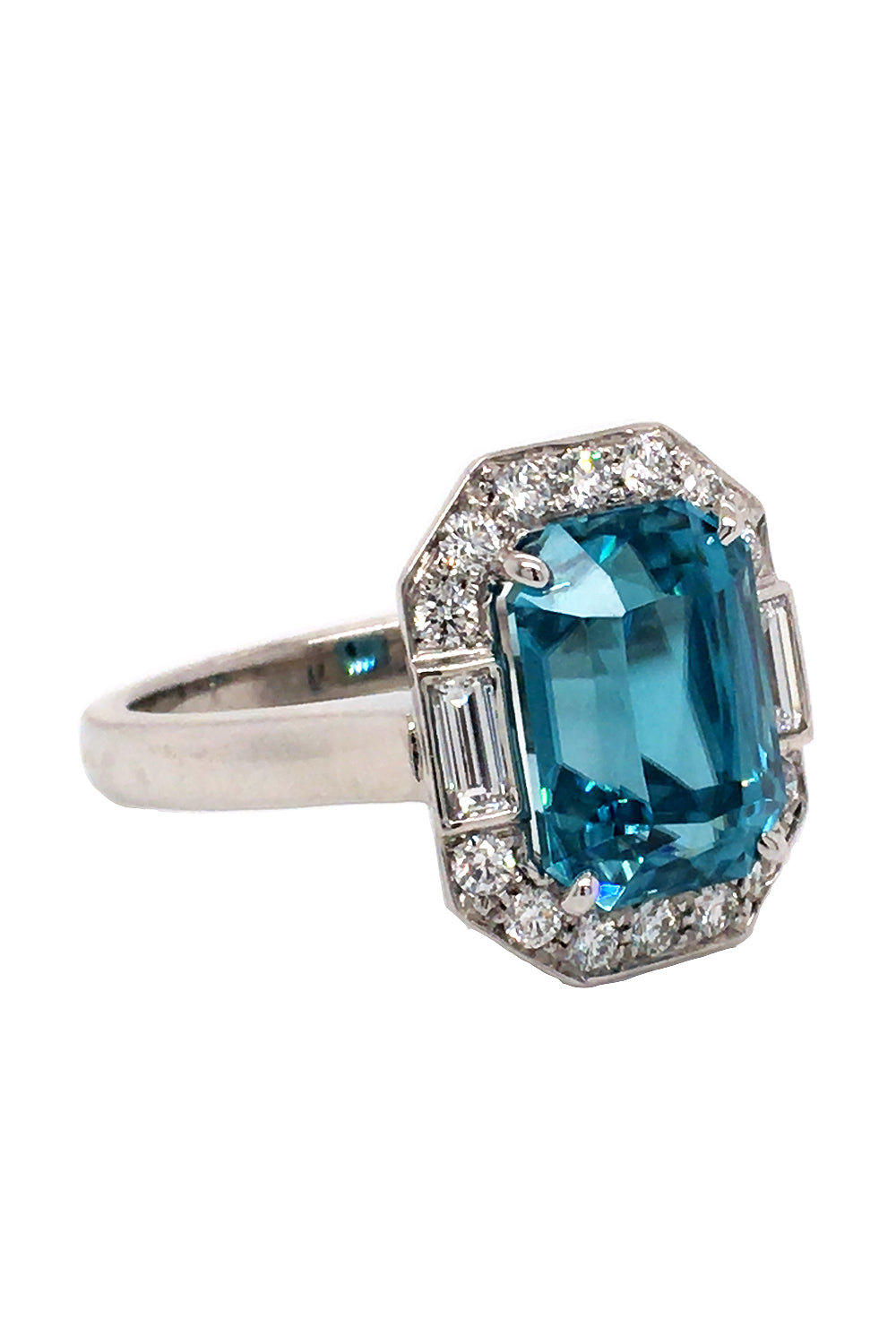 Angle view of 18K white gold ring with an emerald-cut blue zircon and baguette and brilliant  diamonds on a white background