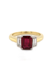 Three-stone ruby ring with two baguette diamonds set in platinum on a yellow gold band on a white background