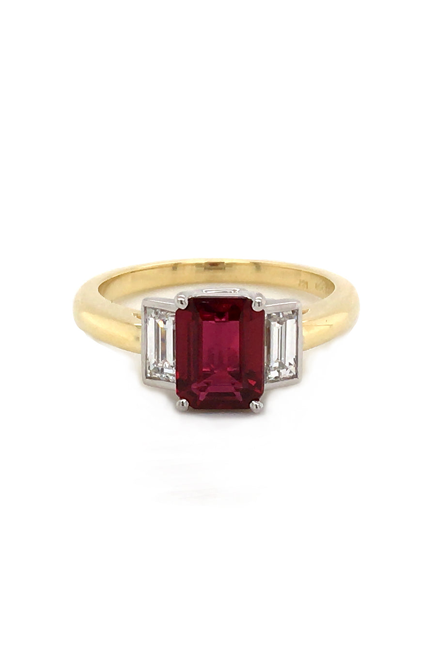 Three-stone ruby ring with two baguette diamonds set in platinum on a yellow gold band on a white background