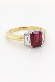 Angle view of three-stone ruby ring with two baguette diamonds set in platinum on a yellow gold band on a white background