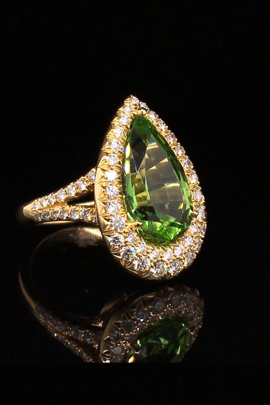 Angle view of 18K yellow gold ring with a pear-shaped peridot and diamond pave on a black background.