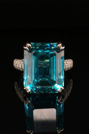 Platinum ring with emerald-cut blue zircon and round diamonds on black background.