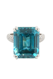 Platinum ring with emerald-cut blue zircon and round diamonds on white background.