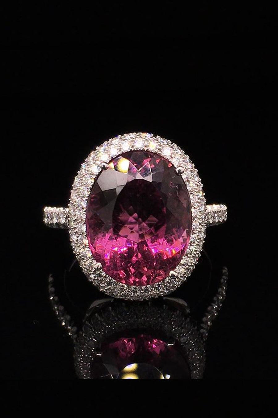 18K white gold ring with a large magenta tourmaline surrounded with diamonds on a black background