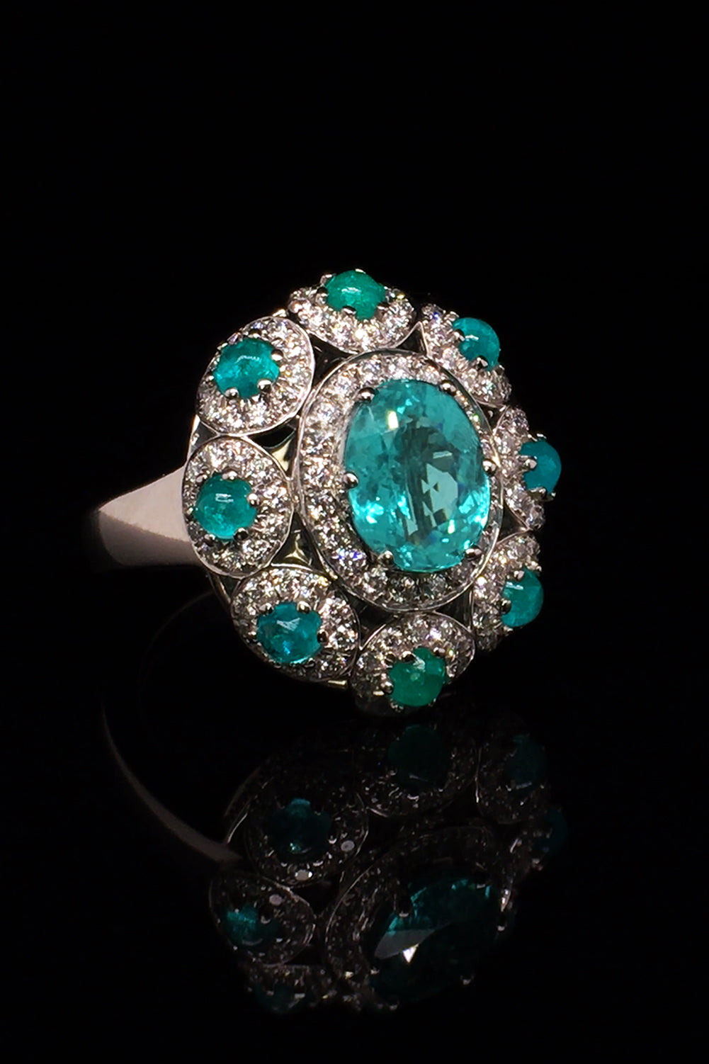 Angle view of platinum ring with a faceted African paraiba, Brazilian cabochon paraibas, and diamonds on a black background