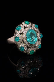 Angle view of platinum ring with a faceted African paraiba, Brazilian cabochon paraibas, and diamonds on a black background