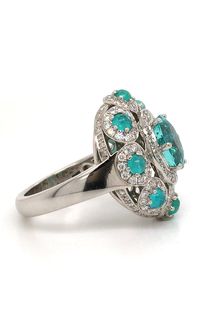 Side view of platinum ring with a faceted African paraiba, Brazilian cabochon paraibas, and diamonds on a white background