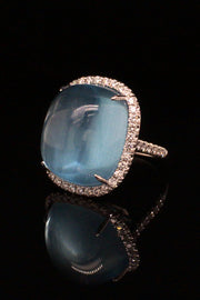 18K white gold ring featuring a large aquamarine cabochon with a diamond halo on black background