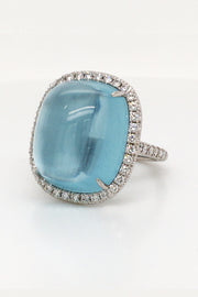 18K white gold ring featuring a large aquamarine cabochon with a diamond halo on white background