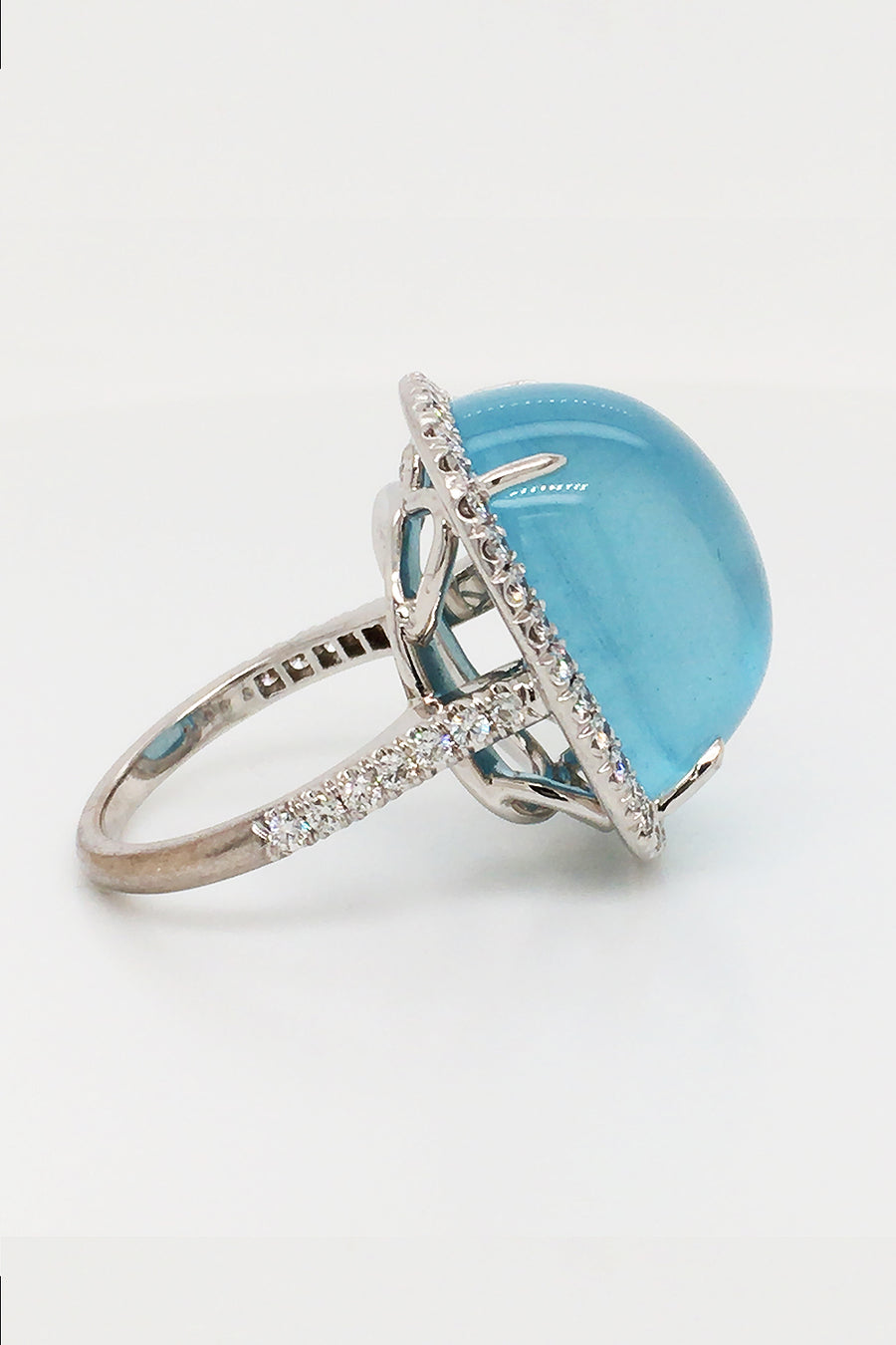 Side view of 18K white gold ring featuring a large aquamarine cabochon with a diamond halo on white background