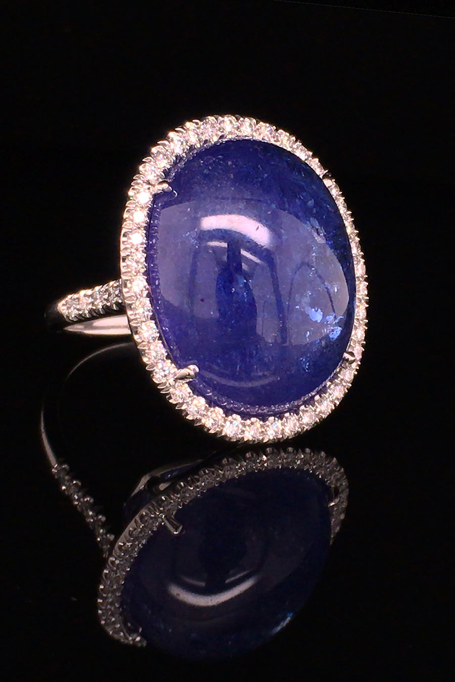 Angle view of an 18K white gold ring with a large oval tanzanite cabochon and diamond halo on a black background