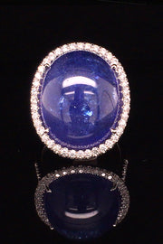 18K white gold ring with a large oval tanzanite cabochon and diamond halo on a black background