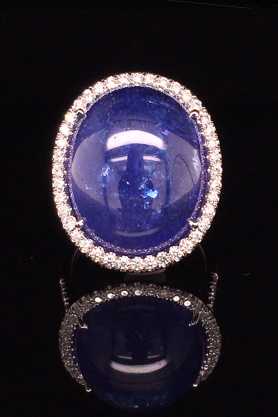 18K white gold ring with a large oval tanzanite cabochon and diamond halo on a black background
