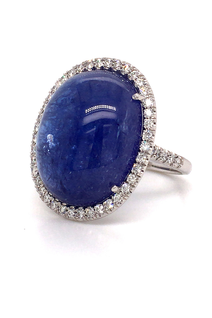 Angle view of an 18K white gold ring with a large oval tanzanite cabochon and diamond halo on a white background