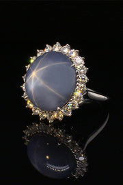 Angle view of platinum ring with large blue-gray star sapphire and brilliant diamonds on a black background.