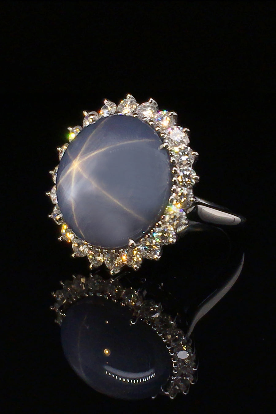 Angle view of platinum ring with large blue-gray star sapphire and brilliant diamonds on a black background.