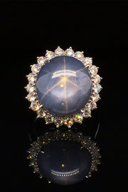 Platinum ring with large blue-gray star sapphire and brilliant diamonds on a black background.