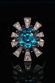 18K white gold ring featuring a blue zircon surrounded by a starburst motif of blue sapphires and brilliant diamonds on a black background.