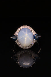 Platinum ring with a star sapphire with two pear-shaped blue sapphires and diamonds on a  black background.