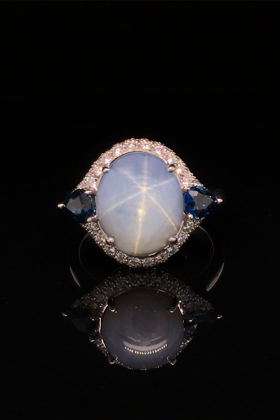 Platinum ring with a star sapphire with two pear-shaped blue sapphires and diamonds on a  black background.