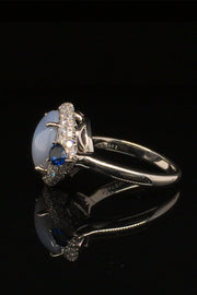 Side view of platinum ring with a star sapphire with two pear-shaped blue sapphires and diamonds on a black background.