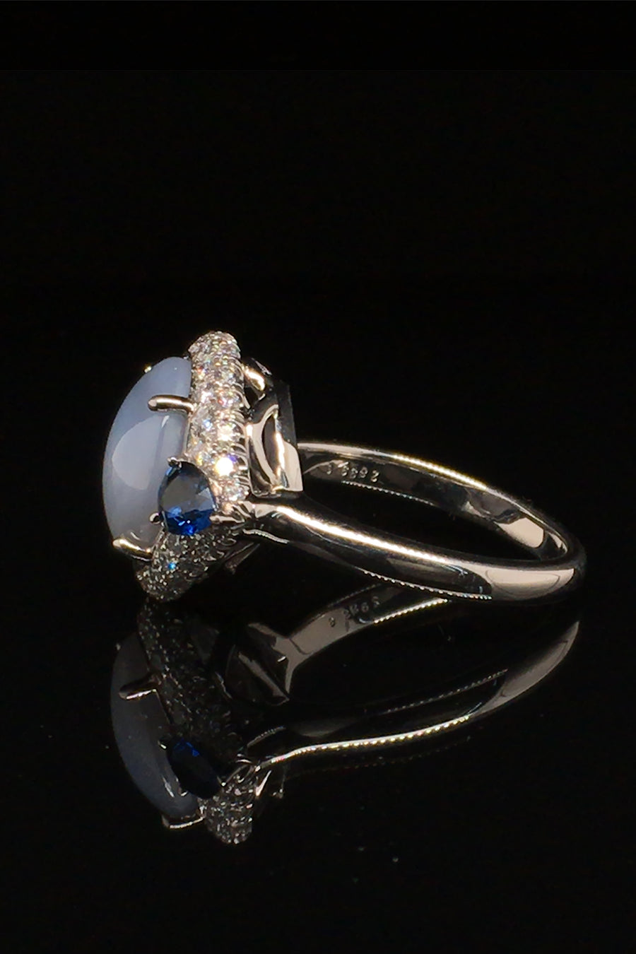 Side view of platinum ring with a star sapphire with two pear-shaped blue sapphires and diamonds on a black background.