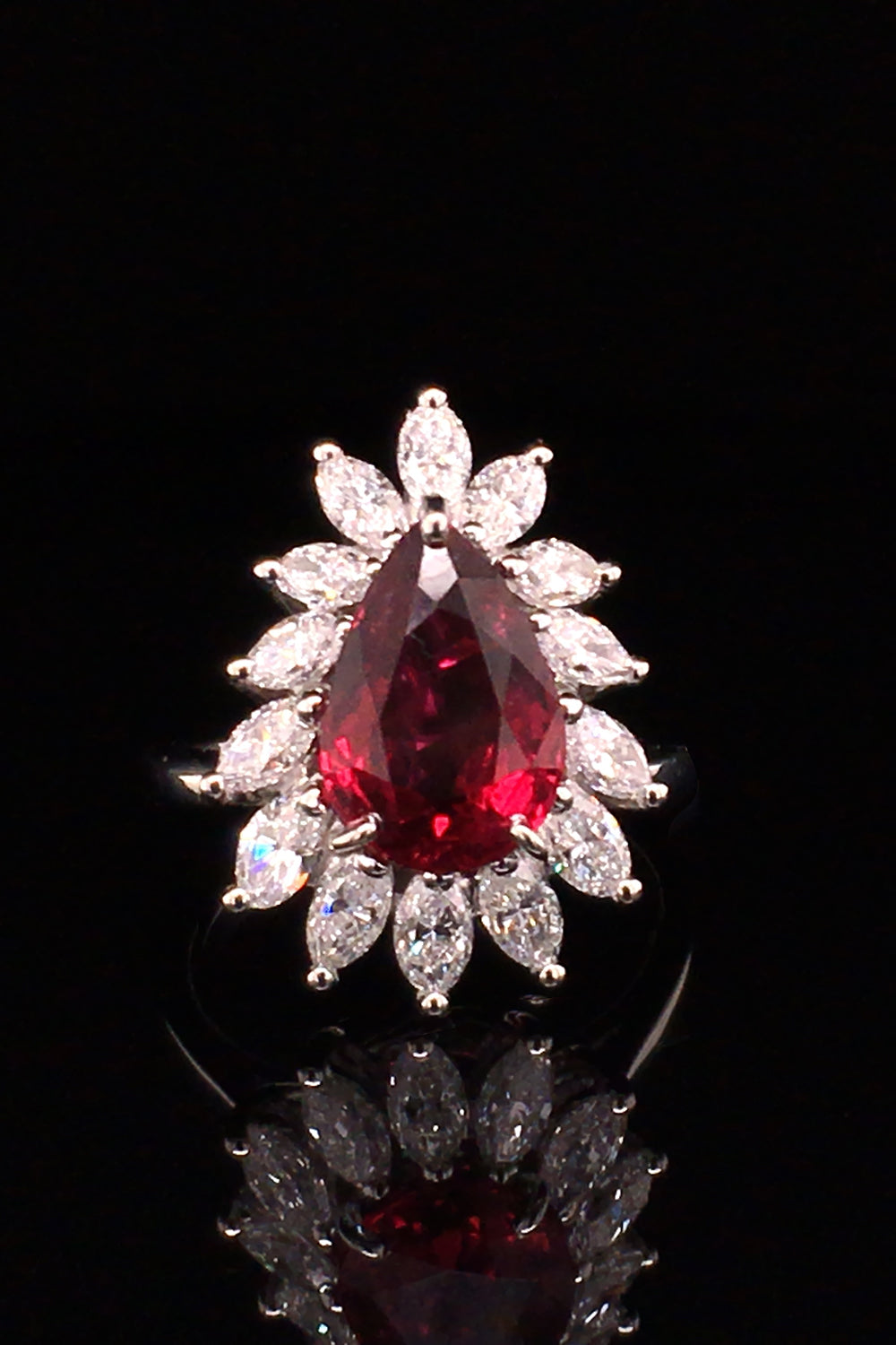 Pear-shaped ruby with marquise diamonds set in platinum on black background.