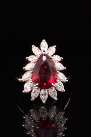 Pear-shaped ruby with marquise diamonds set in platinum on black background.