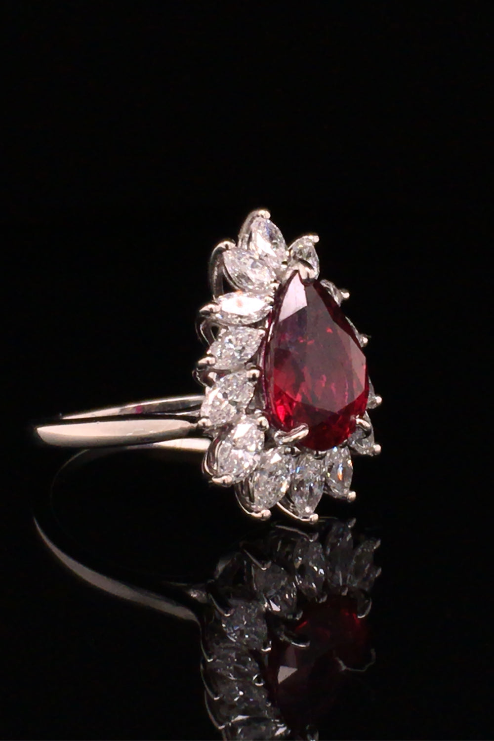 Angle view of pear-shaped ruby with marquise diamonds set in platinum on black background.