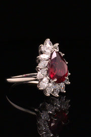 Angle view of pear-shaped ruby with marquise diamonds set in platinum on black background.