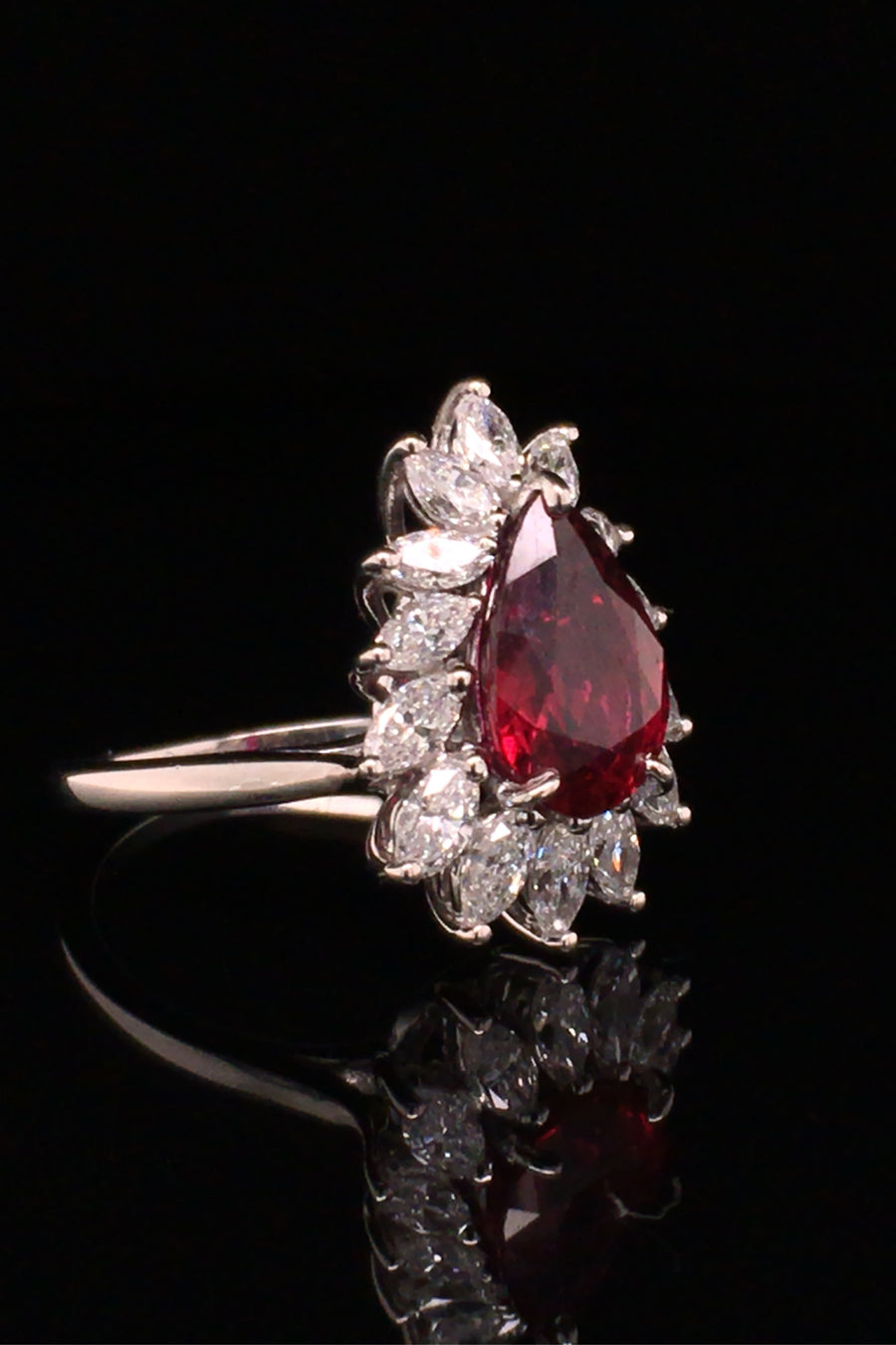 Angle view of pear-shaped ruby with marquise diamonds set in platinum on black background.