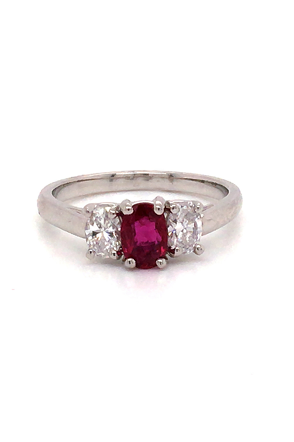 Platinum three-stone ring with a oval ruby flanked by two oval diamonds on a white background.